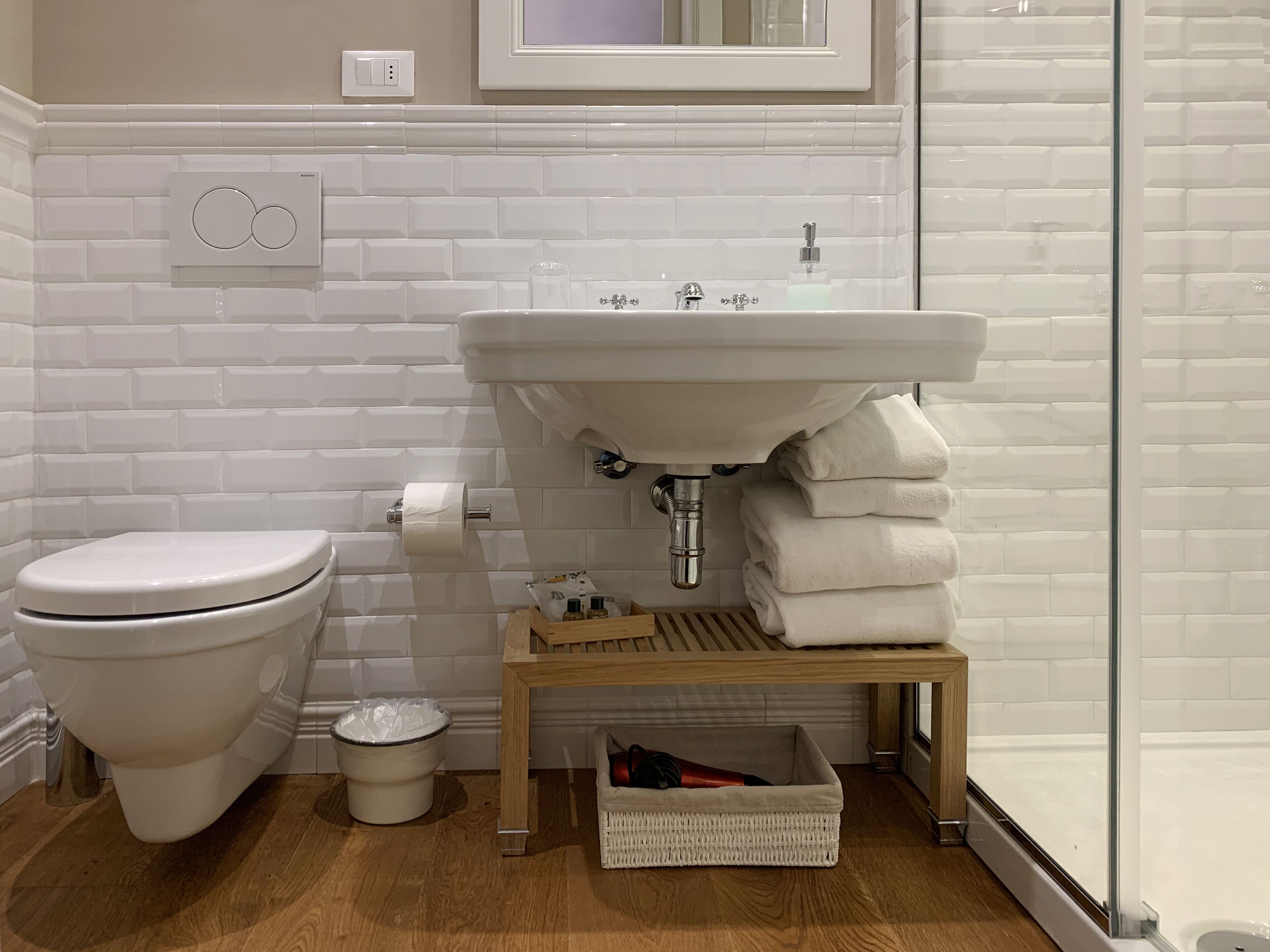 A bathroom with a toilet, sink, and a small wooden shelf with towels.