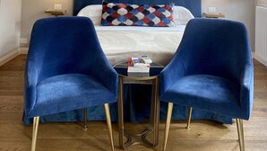 A bedroom with a large bed, two blue armchairs, a small table, and a wooden ceiling with exposed beams and hanging lights. - Santa Croce Terrace - Luxury nest (Firenze)