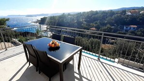 A balcony with a table and chairs, overlooking a scenic view of the sea and hills.