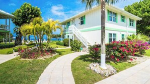 A two-story building with a white exterior and green trim, surrounded by well-maintained gardens and palm trees. - Oceanfront 2 BR & Pool - Cocoplum #5 on 7 Mile (7 Mile Beach)