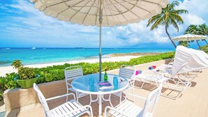 A round table with white chairs and a large umbrella, overlooking a beach with clear blue water and a distant ship. - Oceanfront 2 BR & Pool - Cocoplum #5 on 7 Mile (7 Mile Beach)