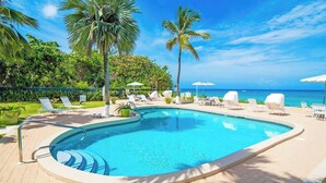 A swimming pool with lounge chairs, palm trees, and a view of the ocean. - Oceanfront 2 BR & Pool - Cocoplum #5 on 7 Mile (7 Mile Beach)