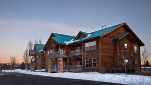 A multi-story wooden lodge with a green roof, balconies, and a parking lot in front.
