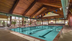 An indoor swimming pool with a wooden ceiling, clear lane dividers, and a lifeguard chair.