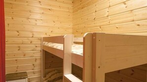 A wooden bunk bed room with a small wooden stool and a red curtain.