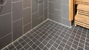 A modern bathroom with grey tiles, a wooden ceiling, and a built-in sauna.