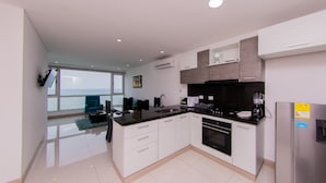 A modern kitchen with white cabinets, a black countertop, and stainless steel appliances. There is a window providing a view of the ocean. - Palmetto Sunset (Cartagena)