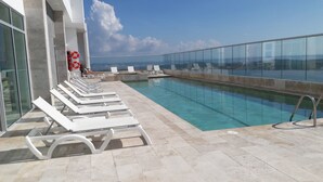 A rooftop pool with white lounge chairs and a clear view of the ocean. - Palmetto Sunset (Cartagena)