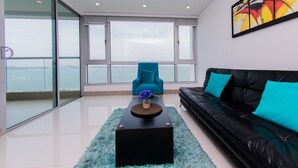 A modern living room with a black leather sofa, a teal armchair, and a black coffee table with a vase of flowers. - Palmetto Sunset (Cartagena)
