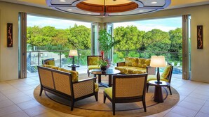 Une pièce spacieuse dotée d’un plafond au design circulaire, de grandes fenêtres offrant une vue sur une végétation luxuriante, et d’une table ronde avec des chaises.