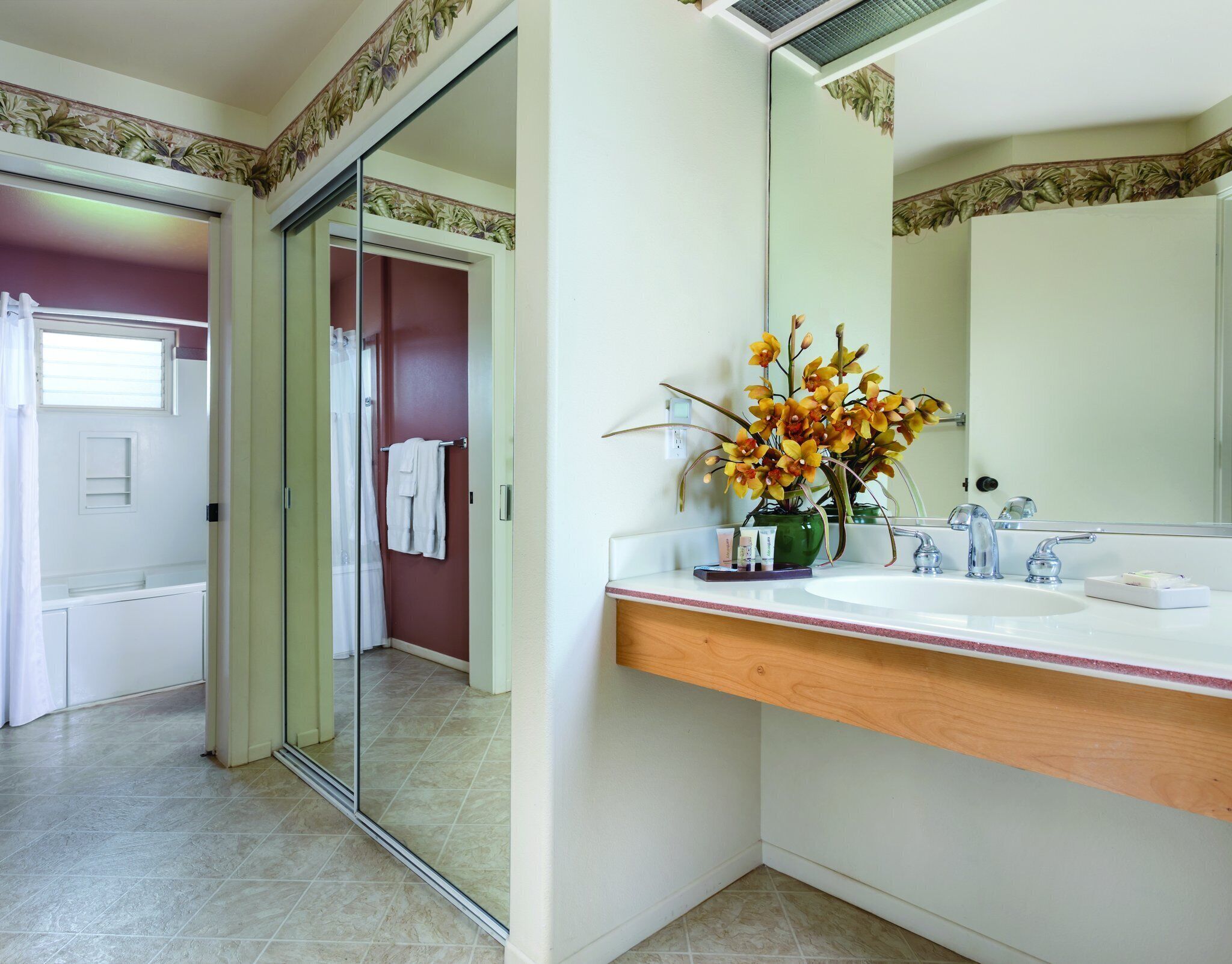 Une salle de bain avec un lavabo blanc, un miroir et un vase rempli de fleurs.