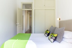 A bedroom with a bed, pillows, a green blanket, a wardrobe, and a hallway leading to a bathroom.