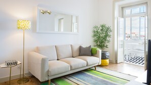Ein modernes Wohnzimmer mit einer Couch, einer Stehlampe, einem Spiegel, einem Blumentopf und Blick durch eine Glastür.