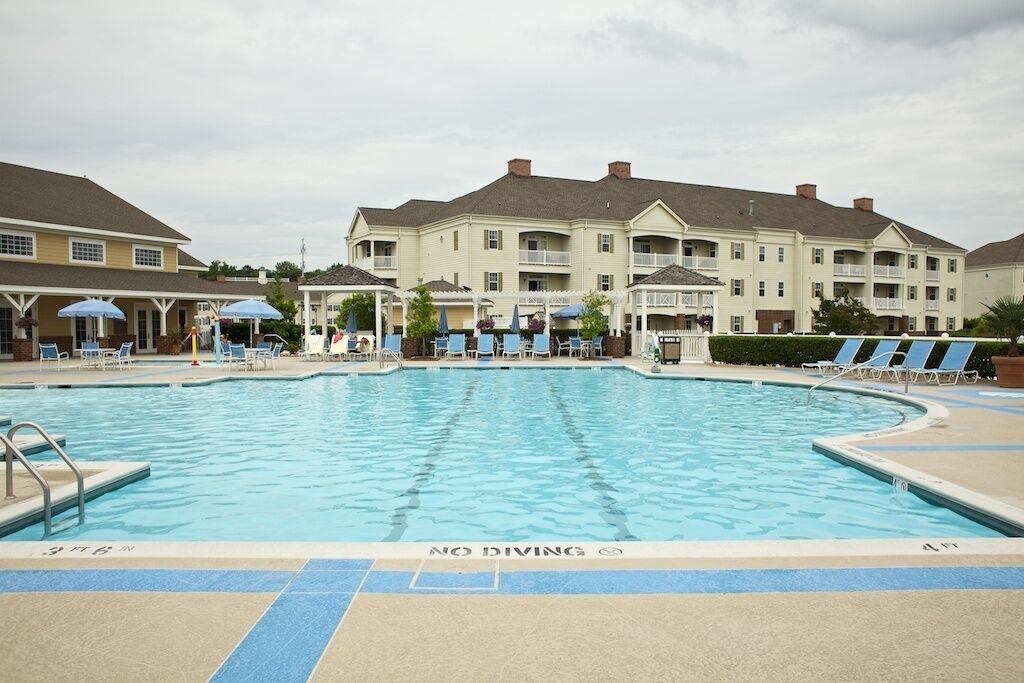 A swimming pool with a 'NO DIVING' sign, surrounded by lounge chairs and umbrellas, with a building in the background.
