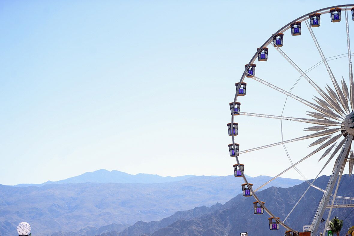 A Ferris wheel with cabins, set against a mountainous backdrop.