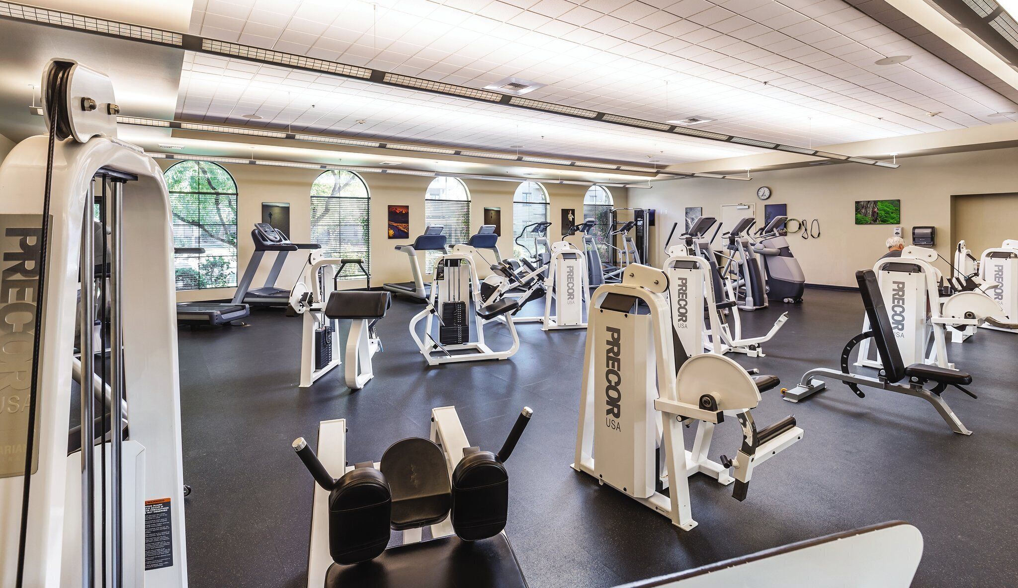 Ett gym med olika träningsmaskiner, stora fönster och ett högt tak.