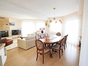 Uma sala de estar espaçosa com uma grande mesa de jantar, assentos confortáveis, uma TV de tela plana e um lustre moderno.