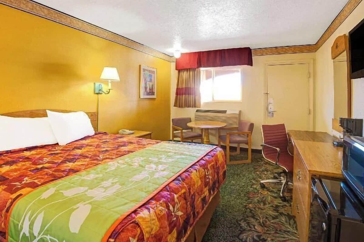 A hotel room with a large bed, a desk with a chair, a television, and a window with curtains.