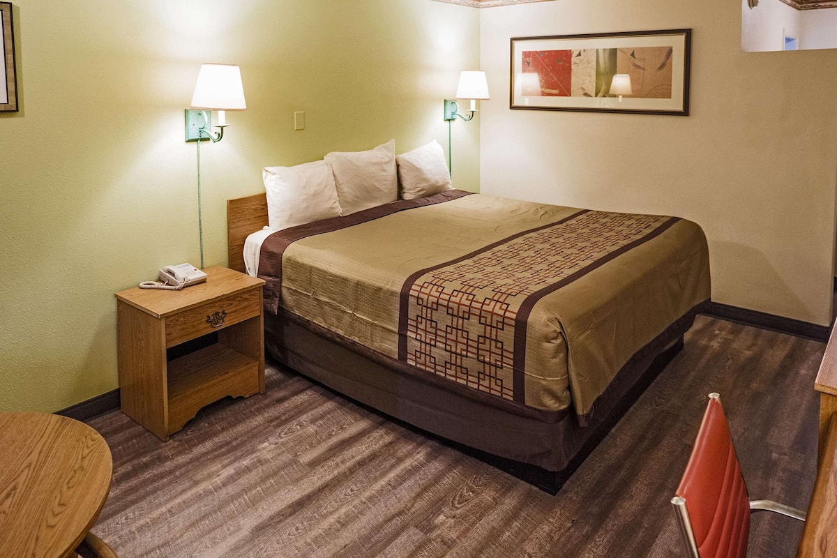 A hotel room with a bed, bedside lamps, a telephone, a small table, and a chair.