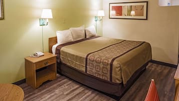 Quarto de hotel com cama, luminárias laterais, telefone, mesinha e cadeira.