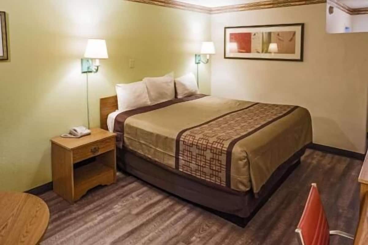 A hotel room with a bed, bedside tables, lamps, a framed picture on the wall, and a carpeted floor.