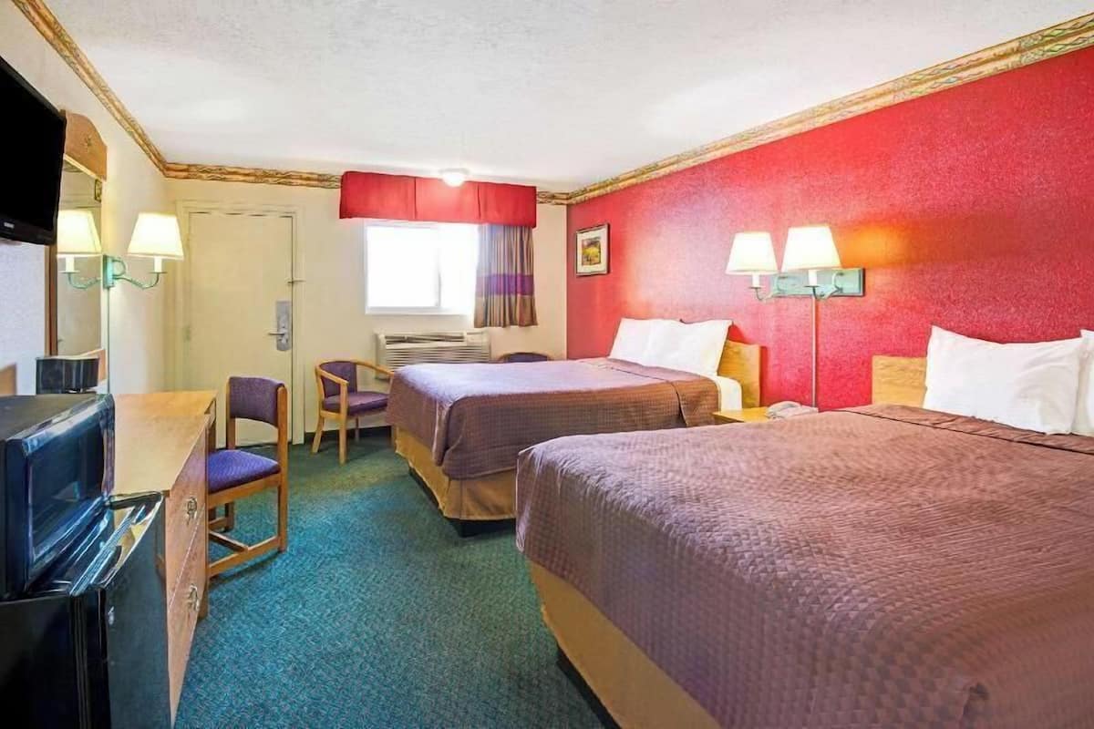 A hotel room with two beds, a desk, a television, and a window with curtains.