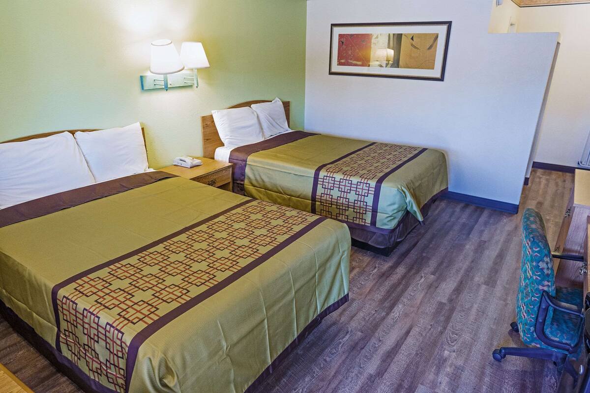 A hotel room with two beds, a desk, a chair, a lamp, and a painting on the wall.