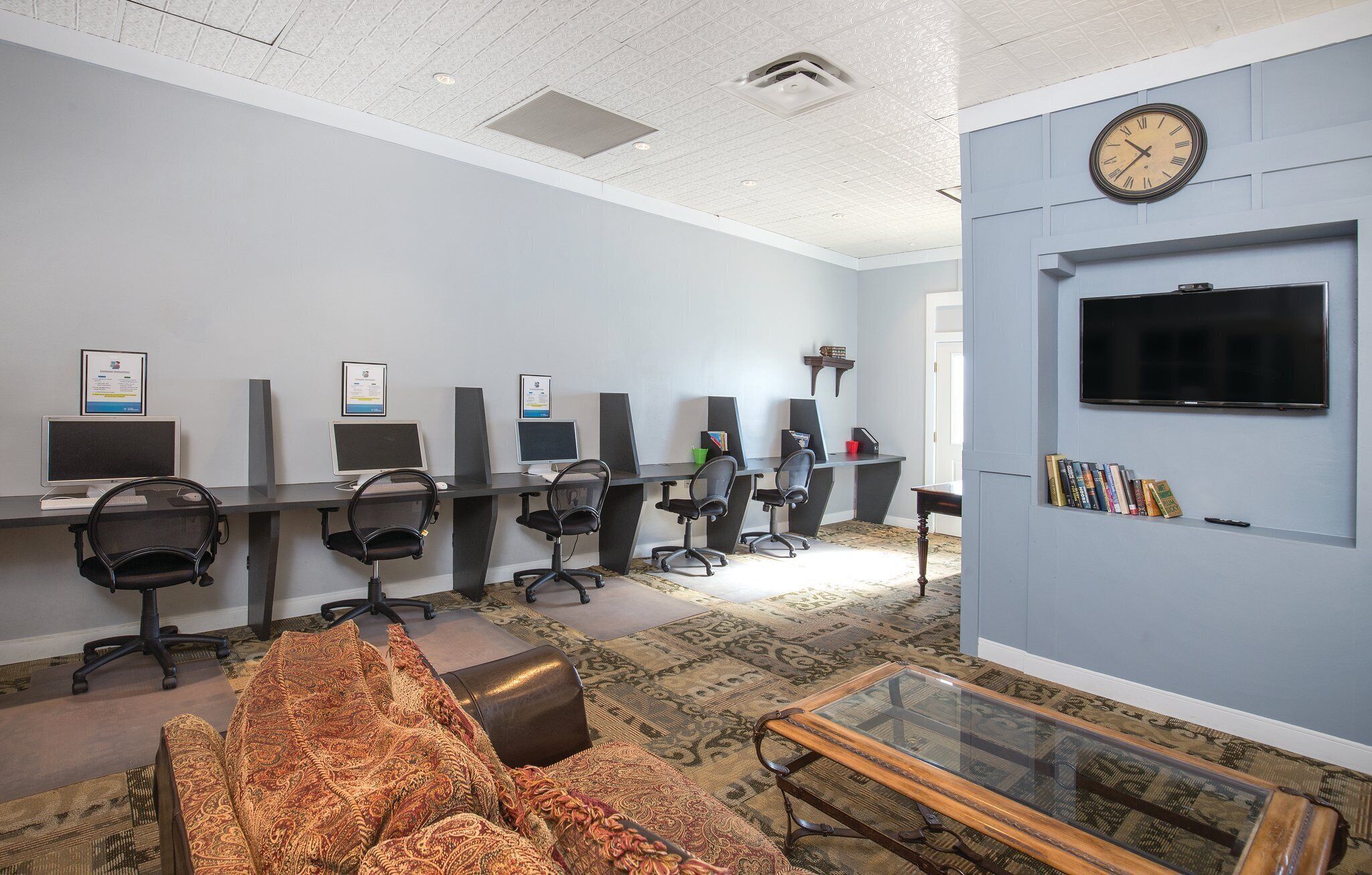 A modern office space with multiple workstations, a television, and a patterned carpet.