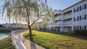 Un edificio residencial con varios balcones, una valla blanca y un árbol en primer plano.
