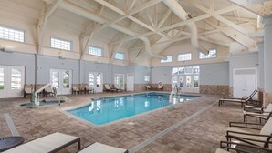 Una piscina interior con vigas de techo transparentes, múltiples salidas y sillones de descanso alrededor de la piscina.