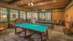 Una sala de billar con múltiples mesas de billar, paredes de madera y ventanas con tonalidad verde.