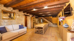 Un interno rustico con una parete in pietra, travi in legno, un divano, un tavolo da pranzo e una scala.