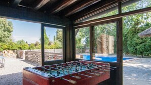 Un tavolo da calcio in un'area esterna coperta con ampie finestre che danno sulla piscina e sul verde.