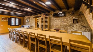 Zona pranzo con un lungo tavolo di legno e sedie, pareti in pietra e una televisione montata a parete.