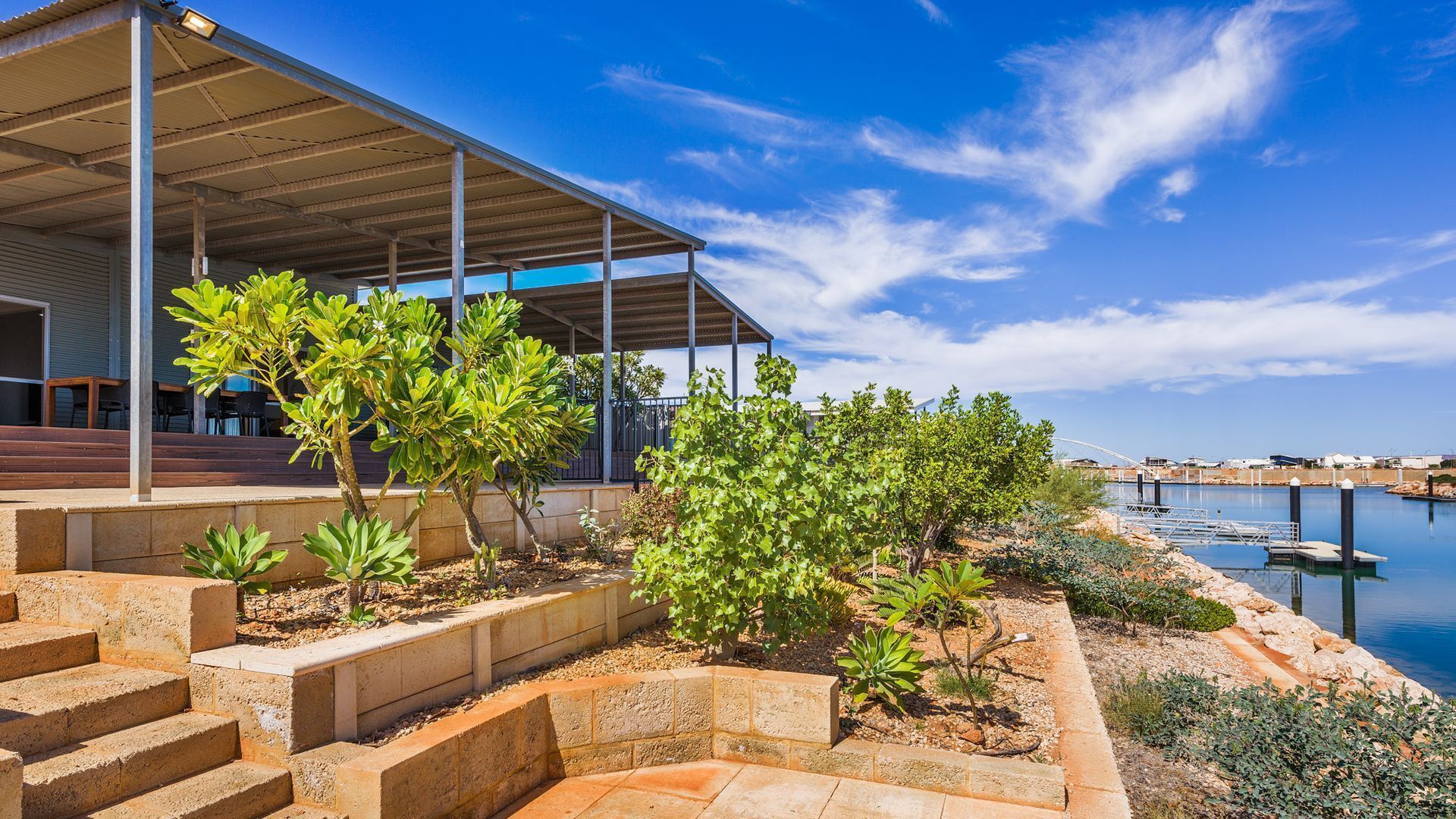 Un bâtiment moderne doté d’un espace extérieur couvert, d’un escalier menant à une terrasse et offrant une vue sur l’eau.