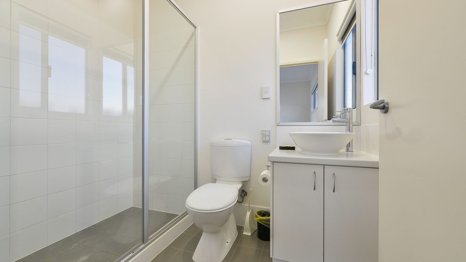 A modern bathroom with a glass shower enclosure, a white toilet, and a sink with a mirror above it.