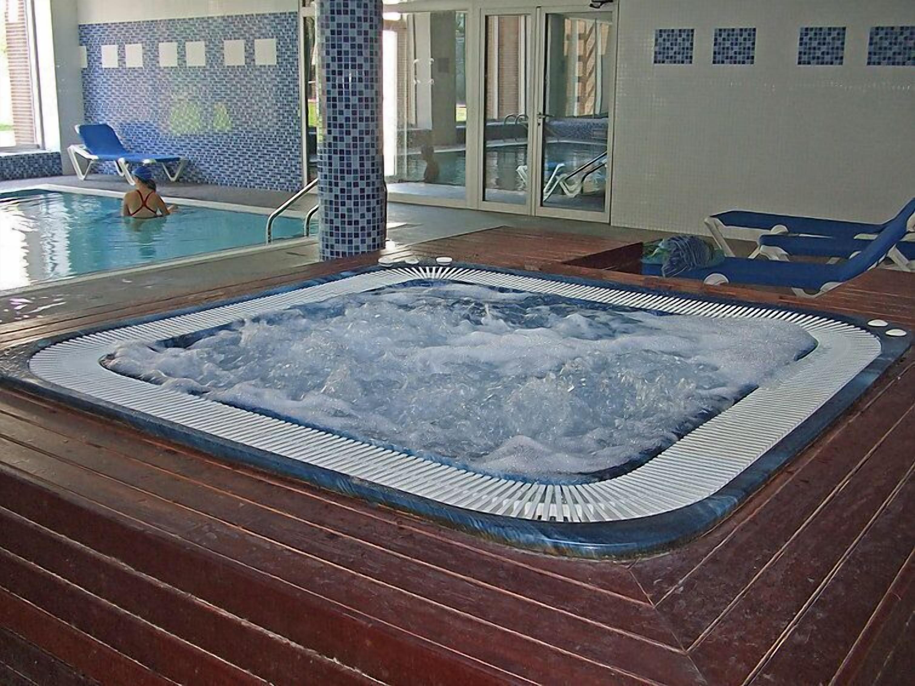 A hot tub with a tiled surround, a pool, and lounge chairs.