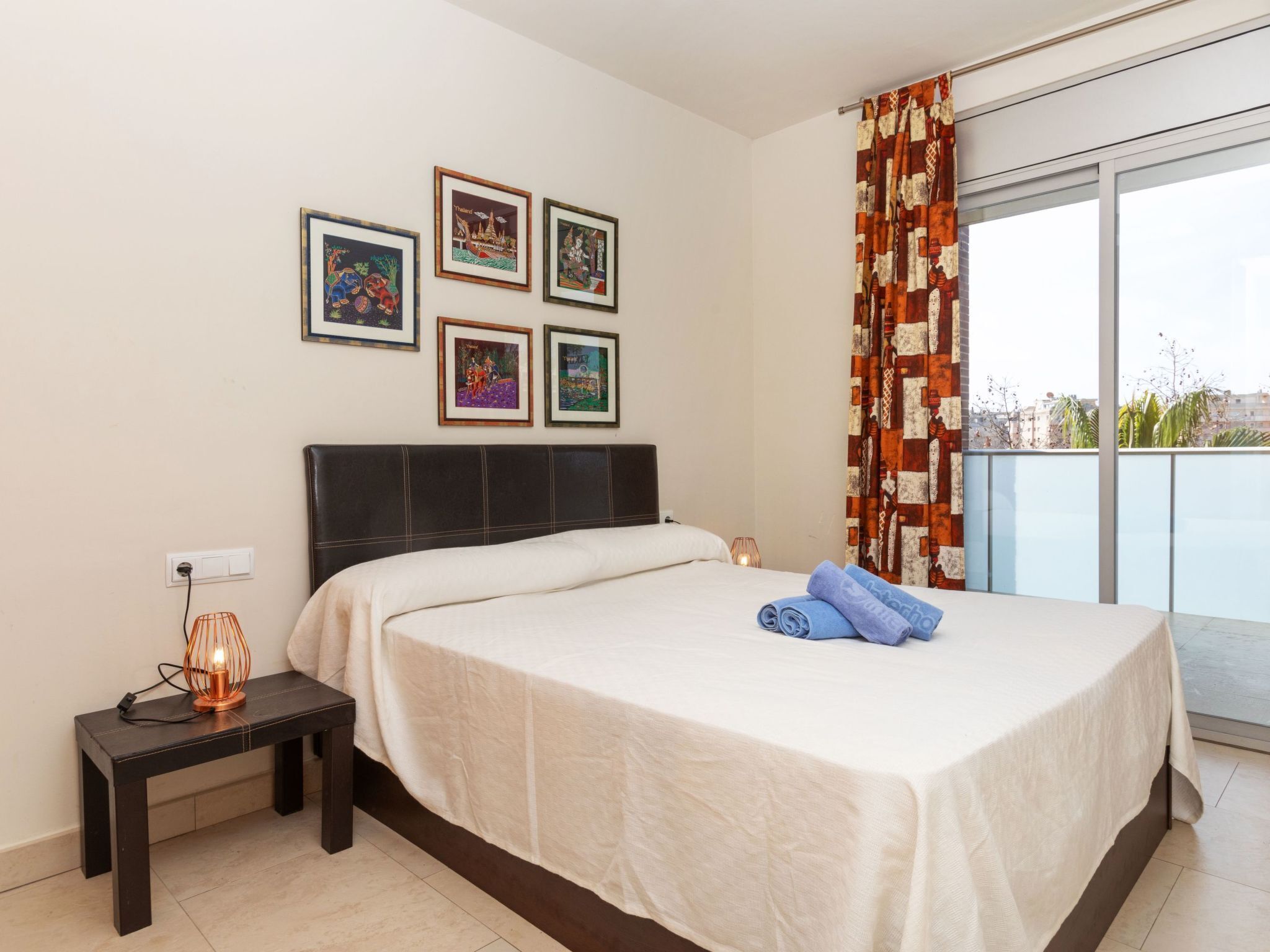 A hotel room with a bed, a nightstand with a lamp, and four framed pictures on the wall.
