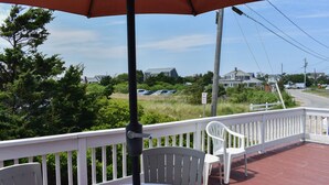 A covered outdoor area with a table and chairs, a white railing, and a view of houses and greenery in the background.