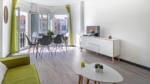 Un soggiorno moderno con un divano, un tavolo da pranzo con sedie, un piccolo tavolino bianco e un televisore su un mobile.