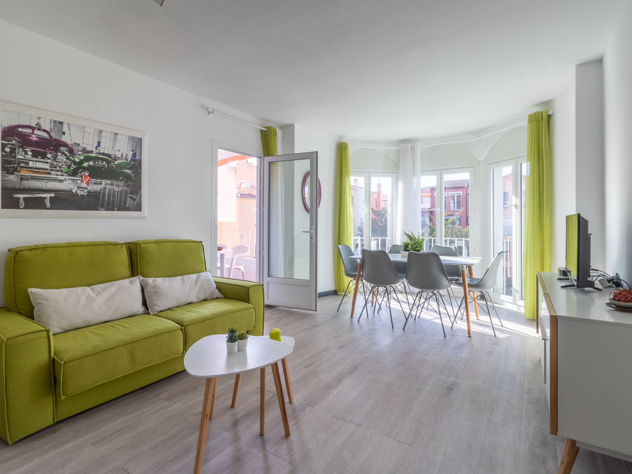 A modern living room with a green sofa, a small white table, and a dining area with chairs and a table.