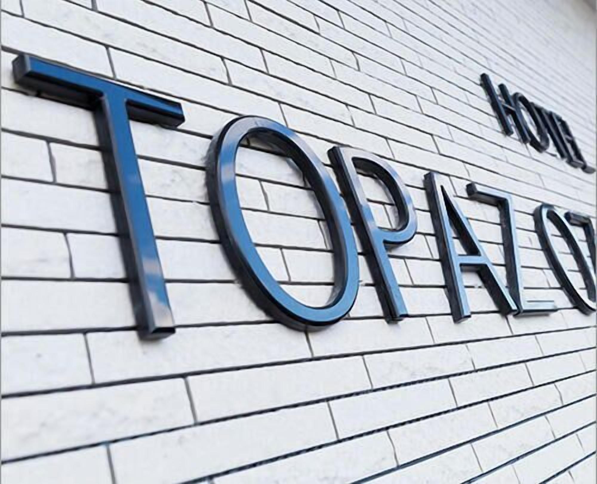 Un letrero de hotel con el nombre "TORAZ" en letras grandes y negritas sobre una pared de ladrillo blanco.