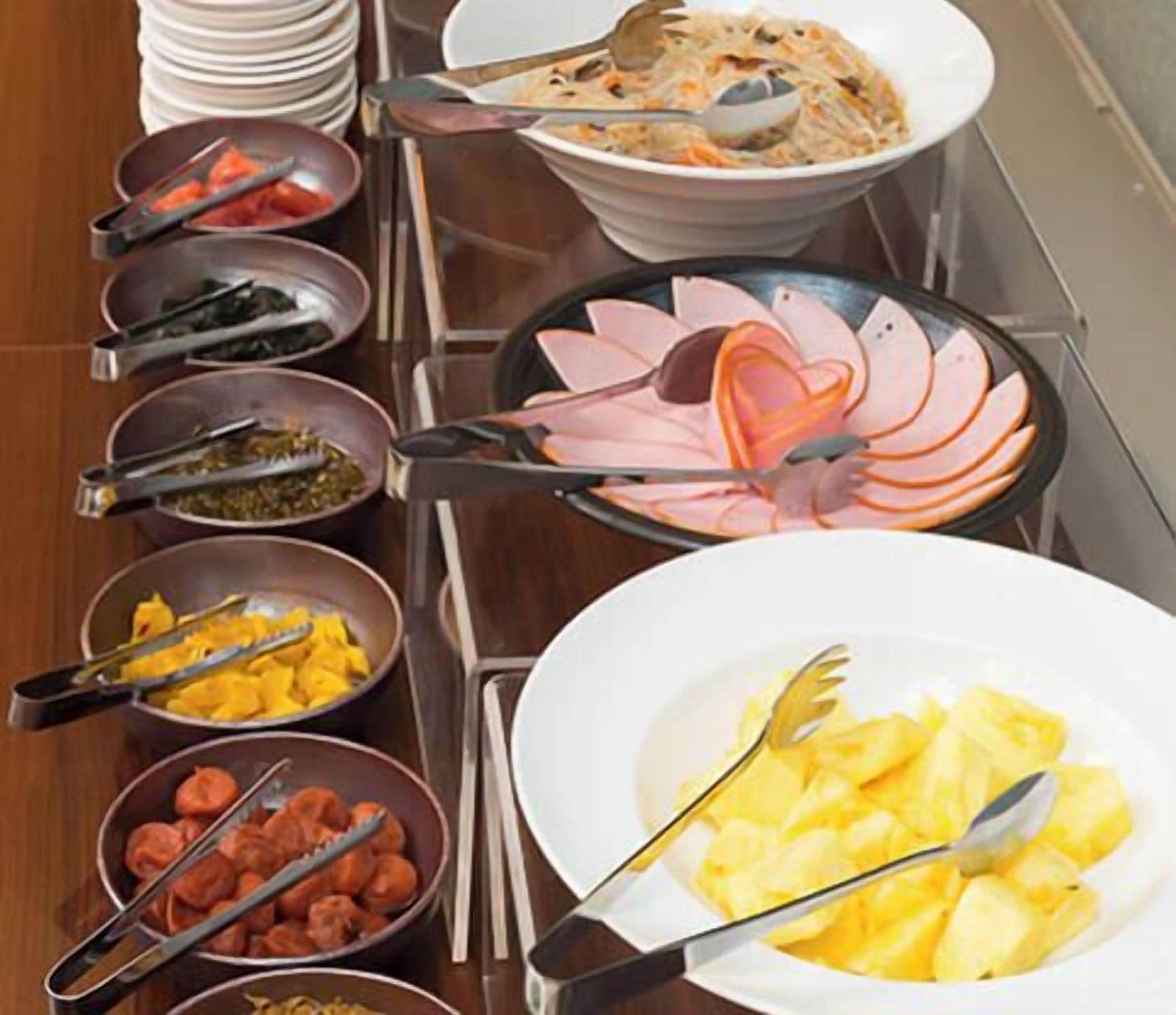 A buffet setup with various dishes including sliced ham, pineapple, and other prepared foods.
