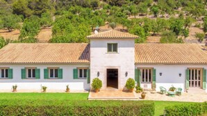 Una casa de dos pisos con techo de tejas, contraventanas verdes y un pequeño porche con mobiliario exterior.