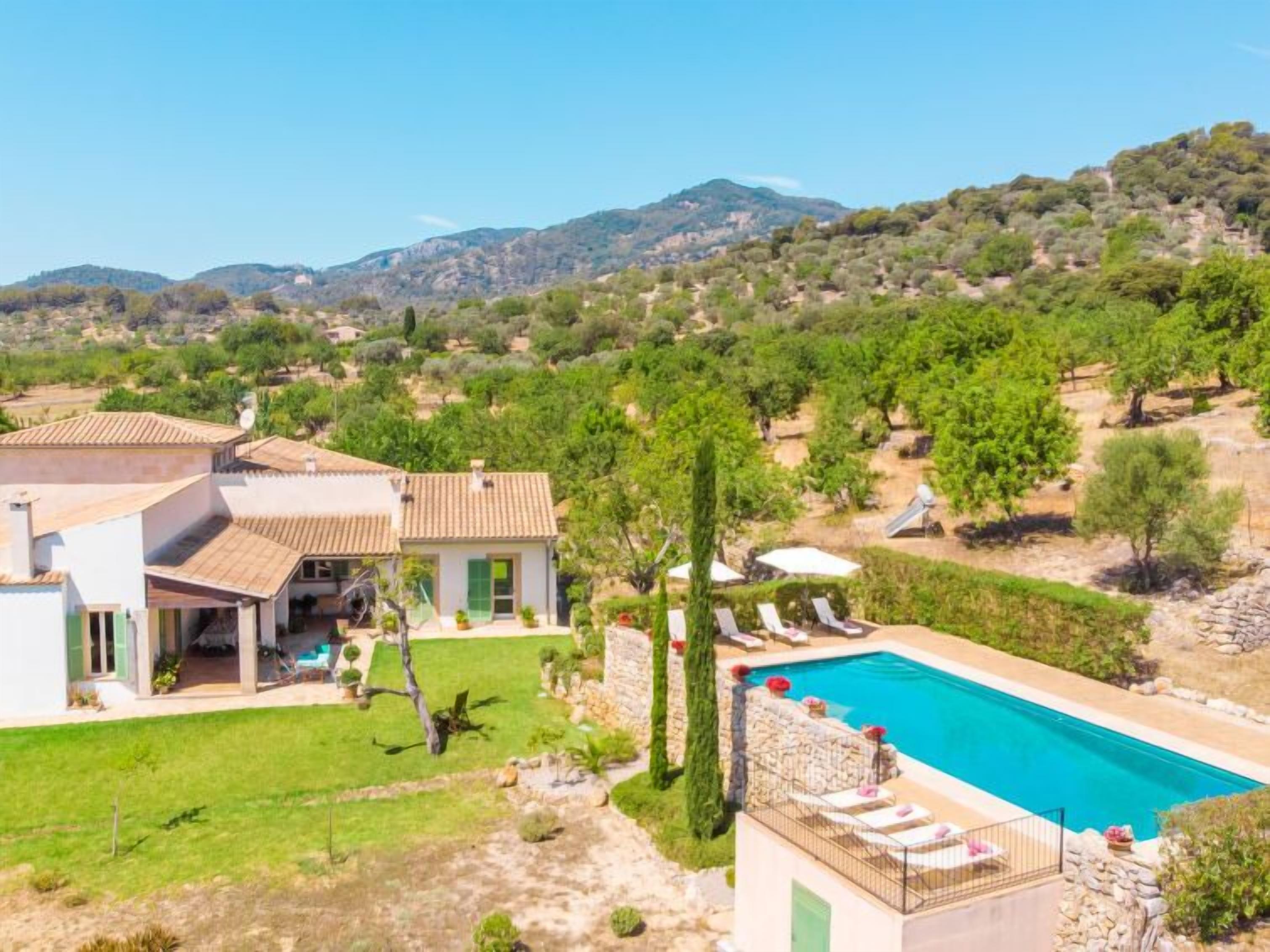 A villa with a swimming pool, a garden, and a view of the surrounding hills.