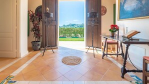 Habitación con vistas a un paisaje verde, una mesa con un libro y flores, y dos lámparas de pie.