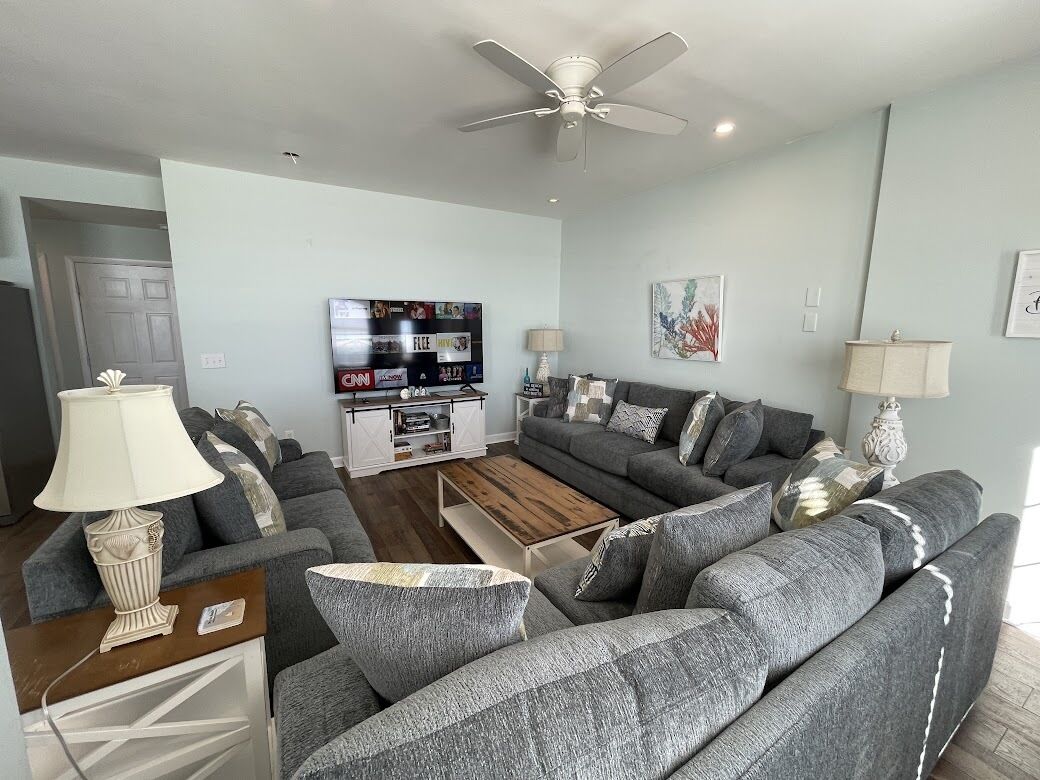 A modern living room with grey sofas, a wooden coffee table, and a ceiling fan.