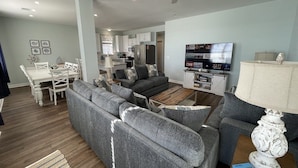A modern living room with a grey sectional sofa, a dining table, and a TV. - Family Seaclusion - Oceanfront in Garden City Beach (Garden City Beach)