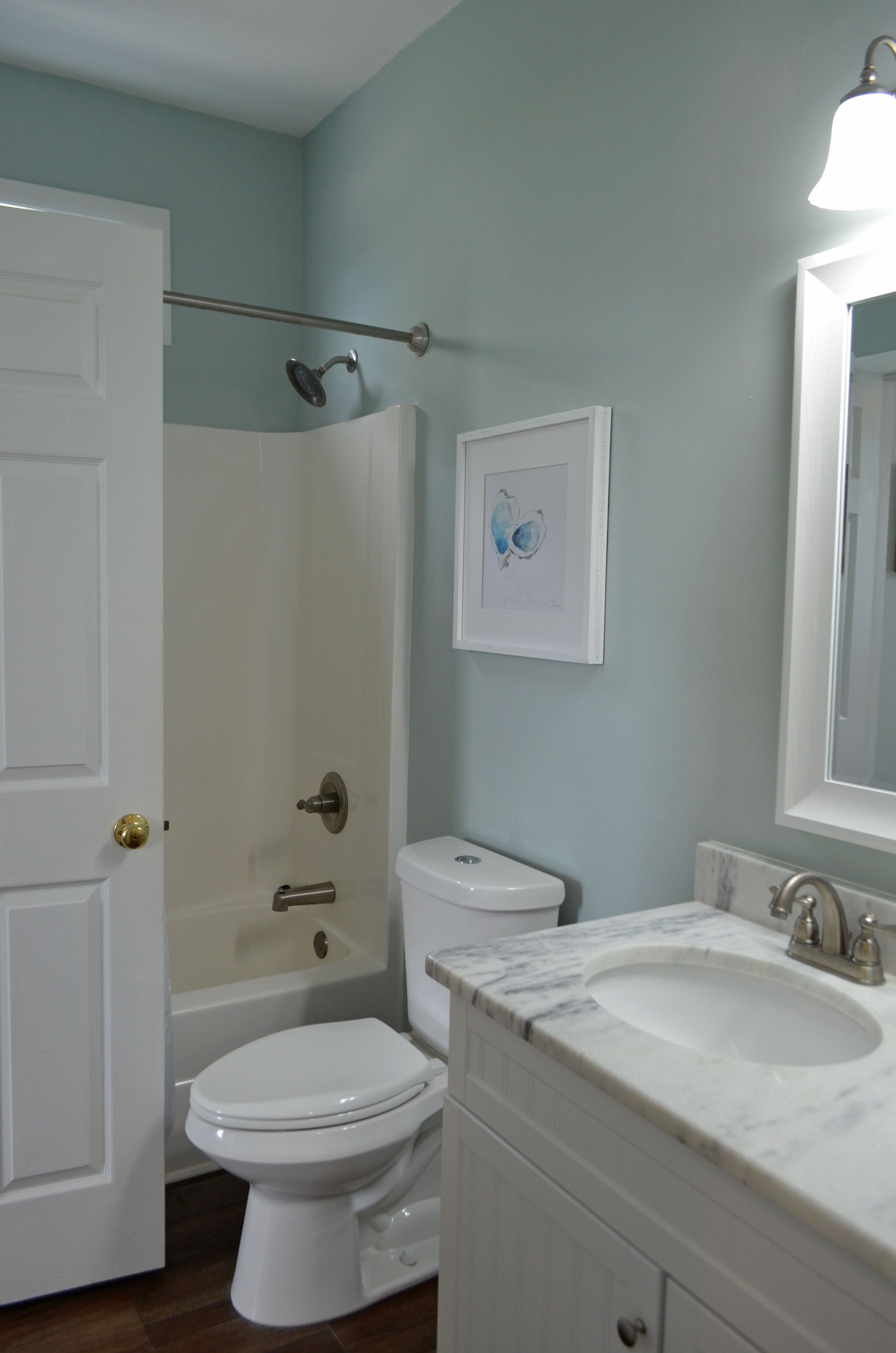 Une salle de bain avec des toilettes blanches, une baignoire, un lavabo doté d’un plan de travail en marbre et un tableau encadré au mur.