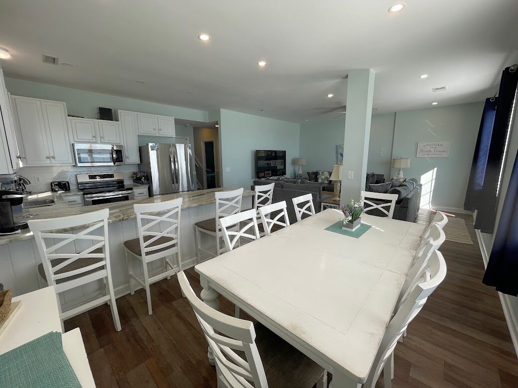 A modern kitchen with white cabinets, a dining area with white chairs, and a central island.